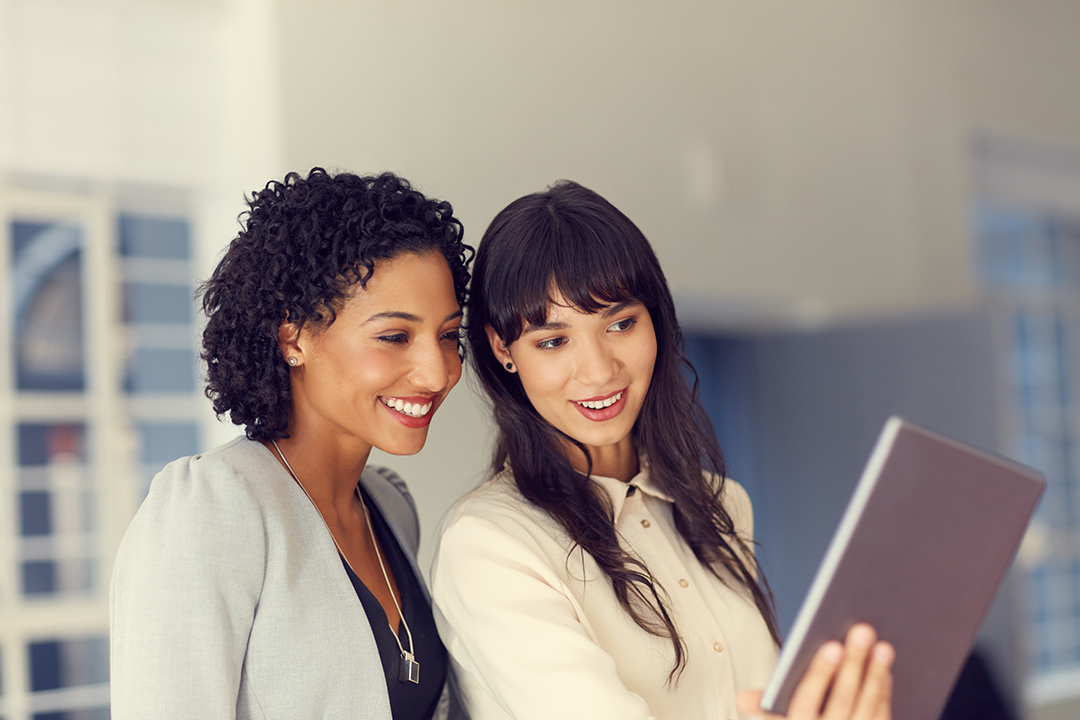 Two women look at a tablet being held by one of them.