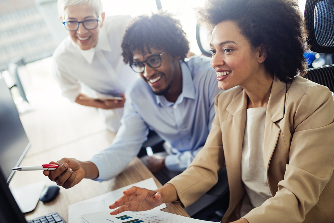 Three people, a person with white hair, a Black man, and a Black woman, face a computer monitor and excitedly discuss what is on screen