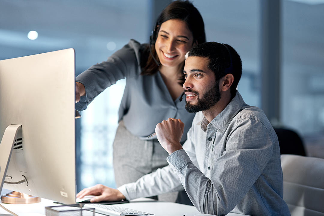 A man and woman look at a computer monitor together.