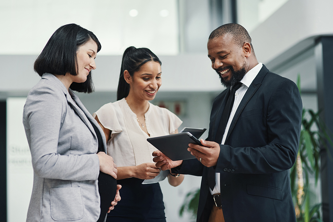 Three people gather around a tablet and smile in conversation
