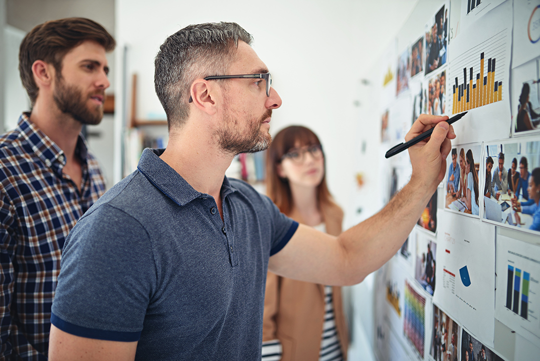 Three people stand in front of a bulletin board with different graphs and photos