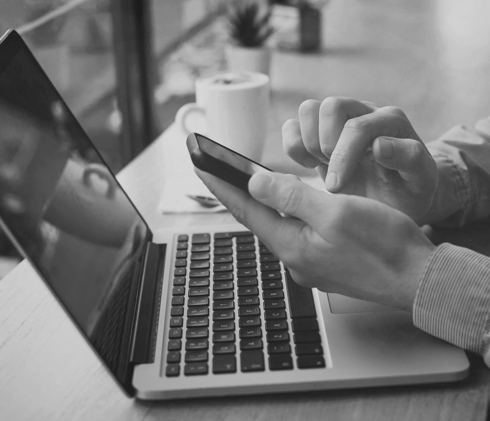 Person scrolling on a cell phone with an open laptop in front of them.